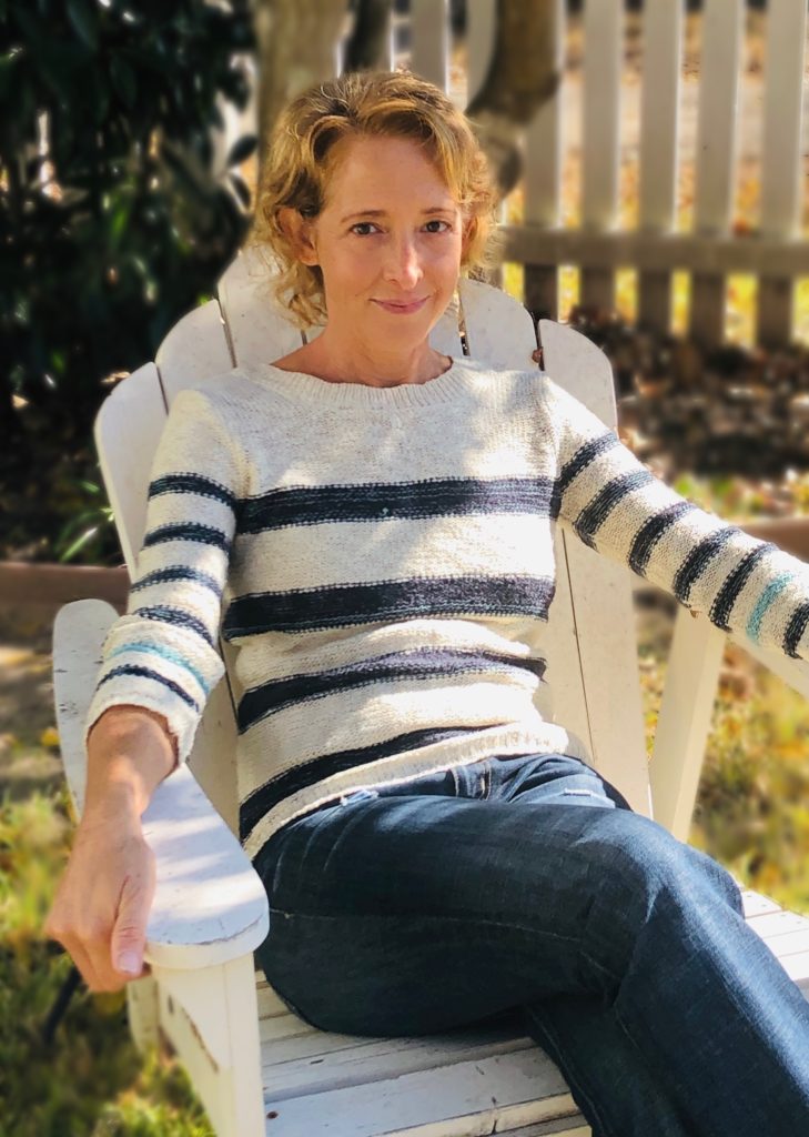 Photo of your life, love and wellness coach, Jennifer Stark, sitting in an adirondack chair smiling at you, ready to listen.