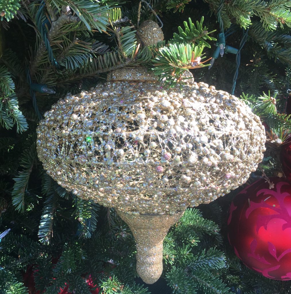 Close up photo of silver ornament on natural Christmas tree outdoors in the  holiday sunshine.