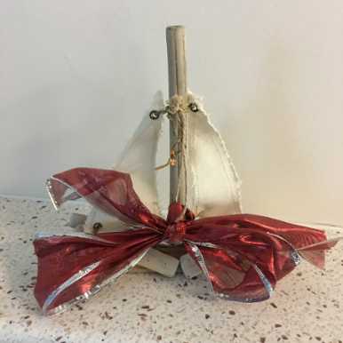 Small sailboat made from driftwood and cotton sails with a Christmas ribbon.
