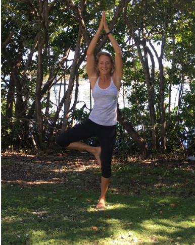Jennifer standing in Tree Pose with a background of tropical trees.